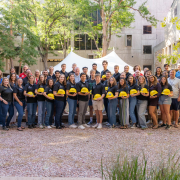 Large group of CU Engineering Kiewit scholars standing in front of engineering building holding a yellow hard hat. 