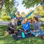 Photo of a group of students sitting on a lawn with a hammock smiling and chatting together.